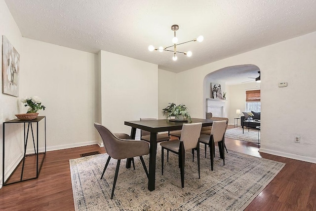 dining room with arched walkways, dark wood-style floors, a textured ceiling, and visible vents