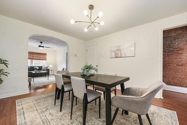 dining space with arched walkways, a textured ceiling, an inviting chandelier, and wood finished floors