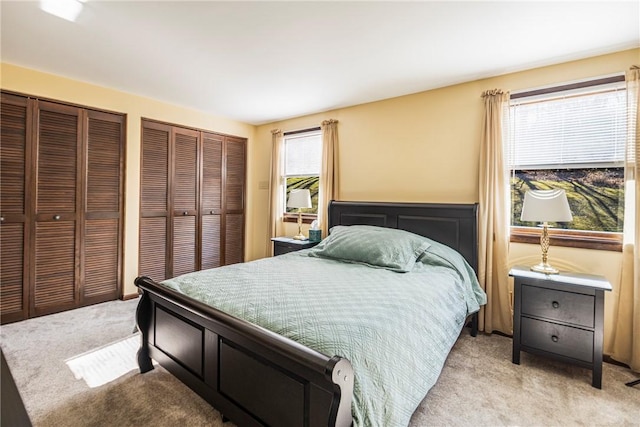 bedroom featuring light colored carpet and multiple closets