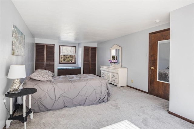 bedroom with baseboards, light carpet, and two closets