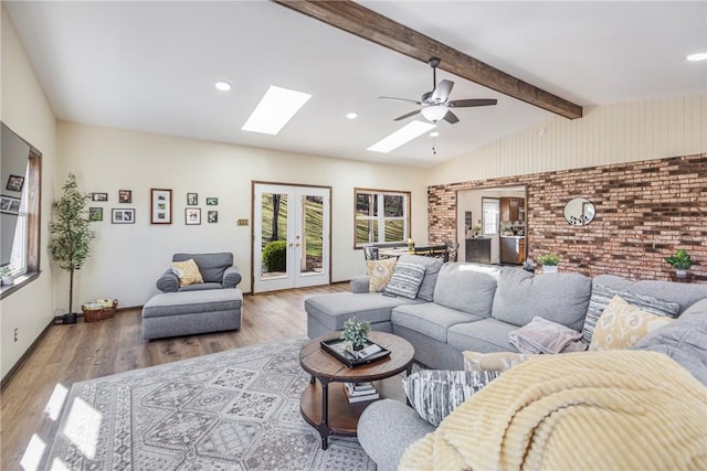 living area with wood finished floors, brick wall, ceiling fan, french doors, and lofted ceiling with skylight