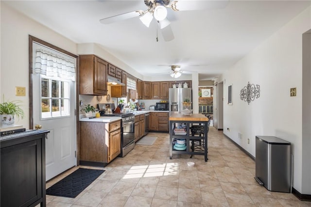 kitchen featuring a ceiling fan, under cabinet range hood, appliances with stainless steel finishes, light countertops, and baseboards