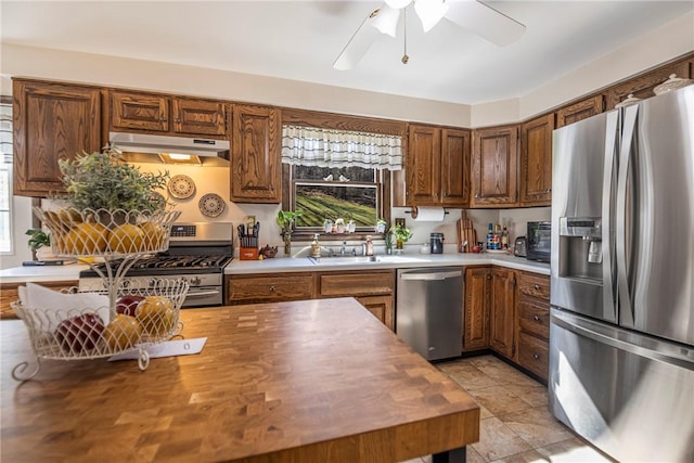 kitchen with butcher block countertops, a ceiling fan, under cabinet range hood, a sink, and stainless steel appliances