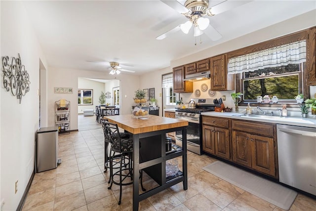 kitchen featuring light tile patterned floors, a ceiling fan, a sink, under cabinet range hood, and appliances with stainless steel finishes