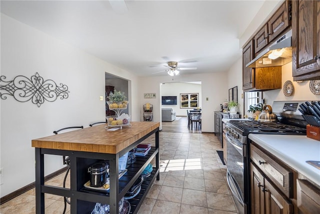 kitchen with baseboards, under cabinet range hood, light countertops, stainless steel gas range, and a ceiling fan