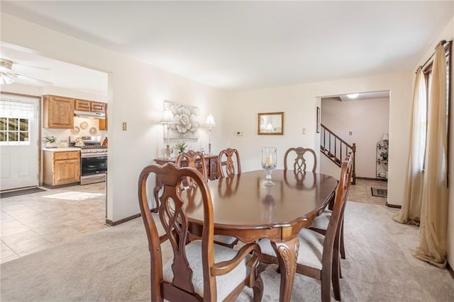 dining area with baseboards, light carpet, a ceiling fan, and stairs