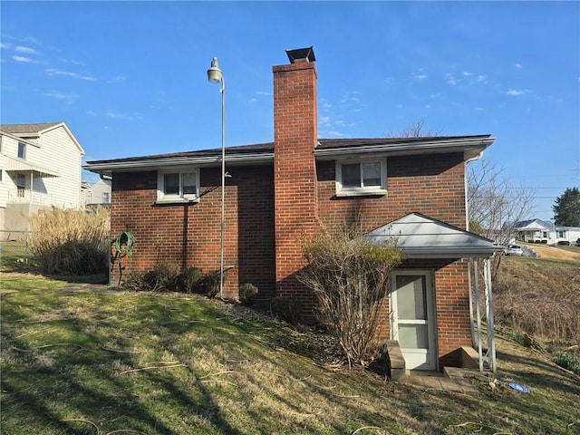 rear view of property with brick siding, a chimney, and a yard