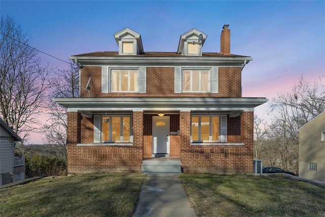 american foursquare style home featuring a chimney, brick siding, covered porch, and a front lawn