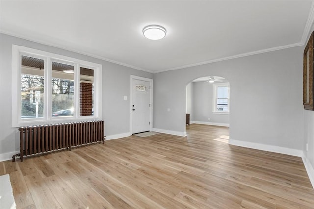 empty room featuring baseboards, light wood-style flooring, radiator heating unit, arched walkways, and crown molding