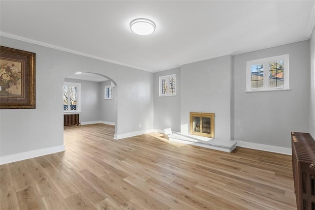 unfurnished living room featuring crown molding, arched walkways, and light wood finished floors