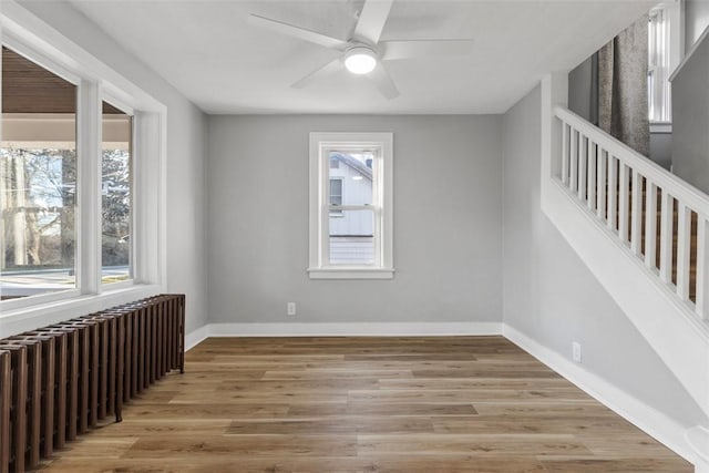 unfurnished room with stairway, radiator, wood finished floors, and baseboards