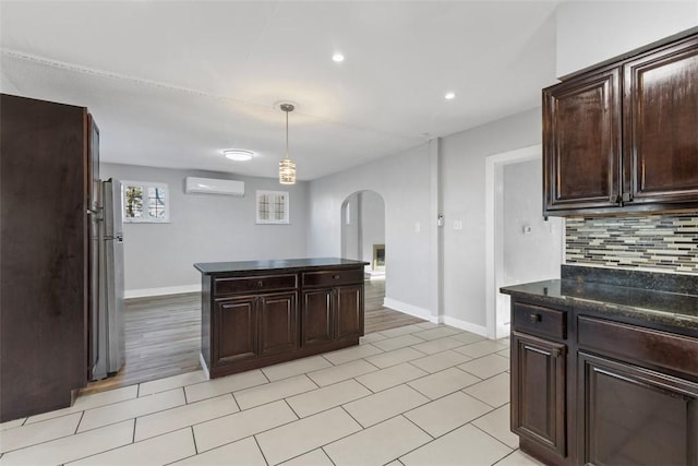 kitchen with tasteful backsplash, dark brown cabinets, a wall unit AC, hanging light fixtures, and arched walkways