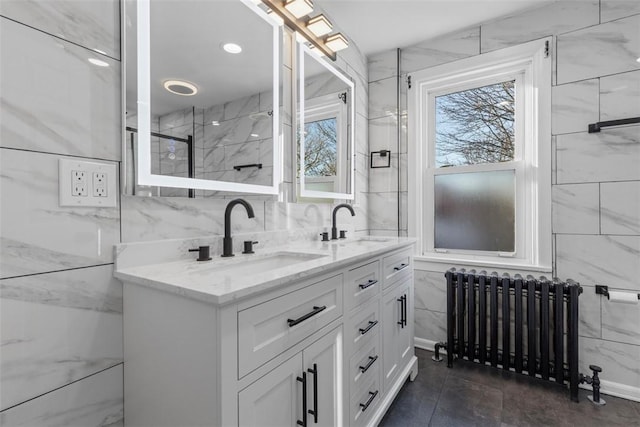 bathroom with double vanity, tile walls, radiator heating unit, and a sink