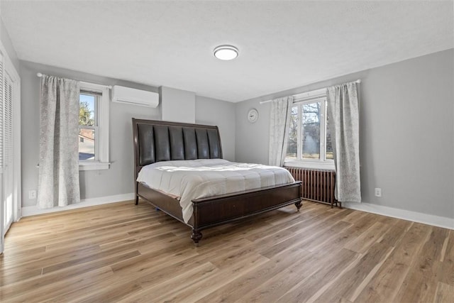 bedroom with baseboards, wood finished floors, radiator heating unit, and a wall unit AC