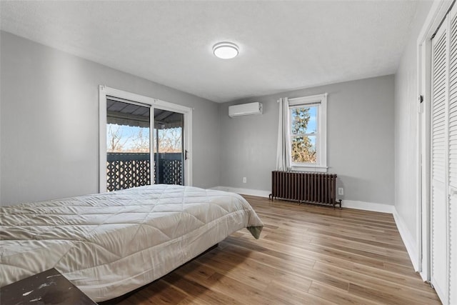 bedroom with multiple windows, radiator, wood finished floors, and a wall mounted AC