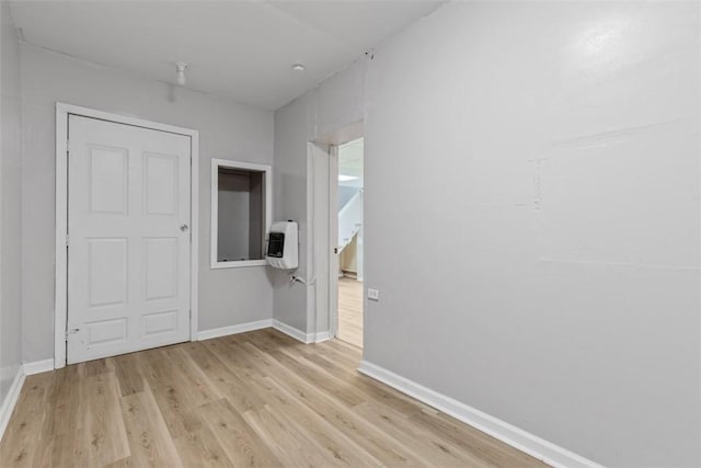 unfurnished room with heating unit, baseboards, and light wood-style floors