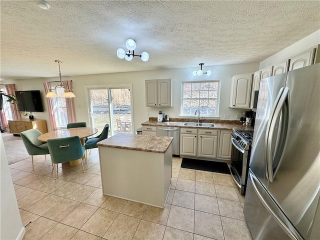 kitchen featuring a healthy amount of sunlight, a kitchen island, light tile patterned flooring, a sink, and appliances with stainless steel finishes