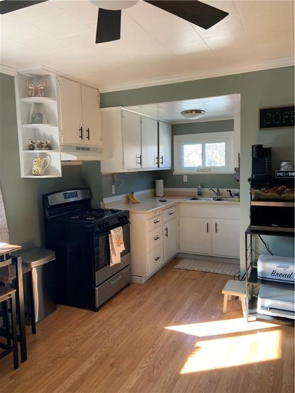 kitchen with under cabinet range hood, light wood-type flooring, light countertops, range with gas stovetop, and a sink