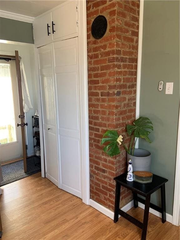 interior space with light wood-style flooring, brick wall, crown molding, and baseboards