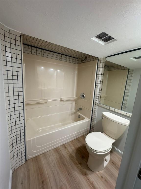 bathroom with visible vents, toilet, a textured ceiling, wood finished floors, and shower / bath combination