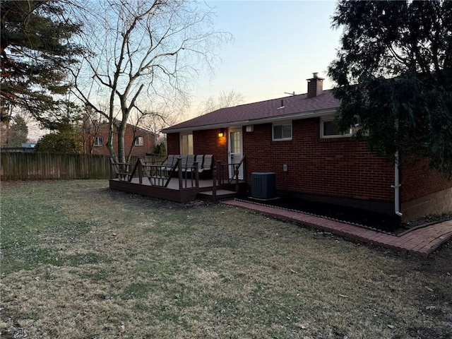 back of property at dusk with fence, a lawn, brick siding, and central AC