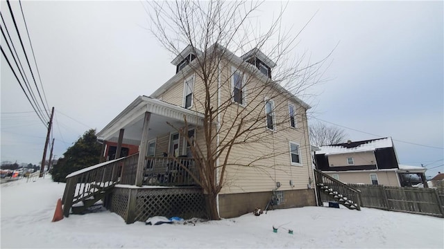 snow covered property with a porch, stairs, and fence