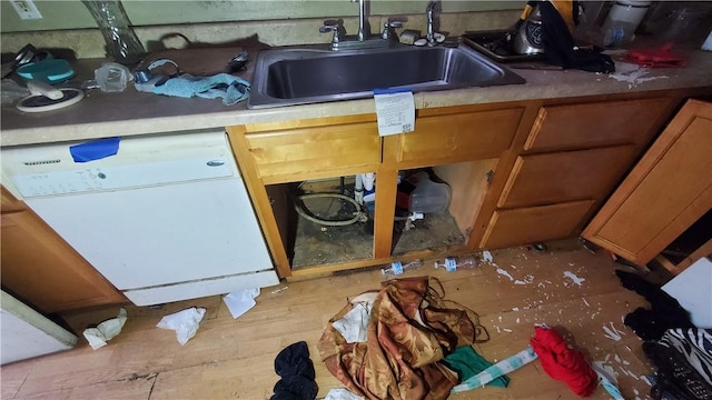 kitchen with brown cabinetry, light wood-style floors, white dishwasher, and a sink