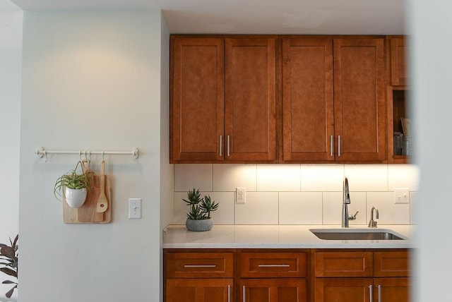 kitchen with brown cabinetry, decorative backsplash, light stone counters, and a sink