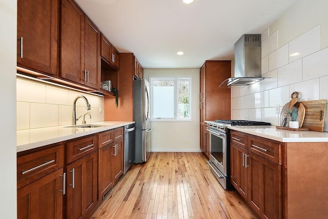 kitchen with light wood-style flooring, a sink, light countertops, appliances with stainless steel finishes, and wall chimney exhaust hood