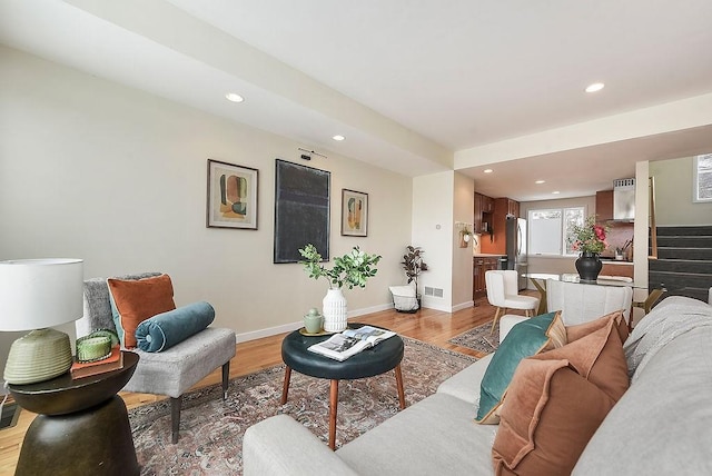 living room with light wood finished floors, visible vents, stairs, and baseboards