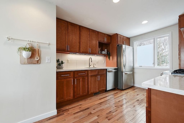 kitchen with light wood-type flooring, a sink, stainless steel appliances, tasteful backsplash, and brown cabinets