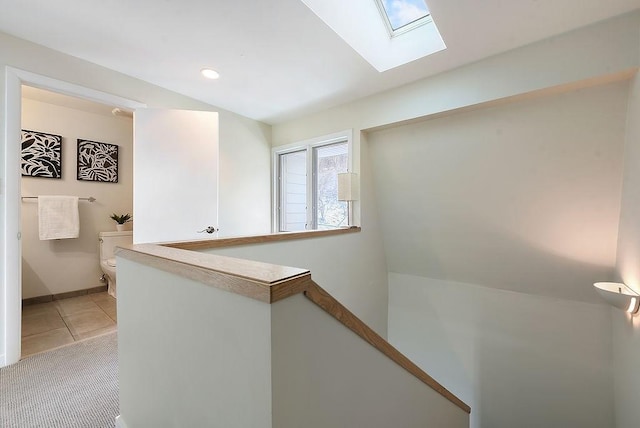 hall with light tile patterned floors, baseboards, an upstairs landing, and a skylight