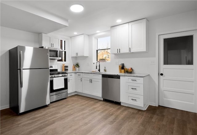 kitchen with a sink, stainless steel appliances, wood finished floors, and white cabinetry