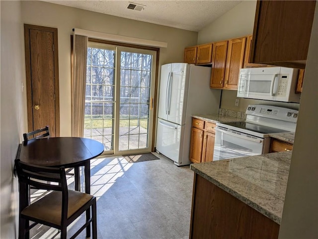 kitchen featuring white appliances, light stone counters, brown cabinetry, visible vents, and a textured ceiling