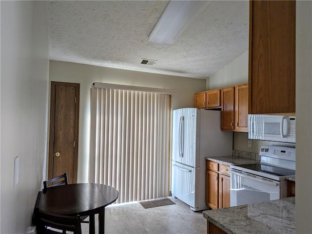 kitchen featuring visible vents, stone countertops, a textured ceiling, white appliances, and brown cabinetry