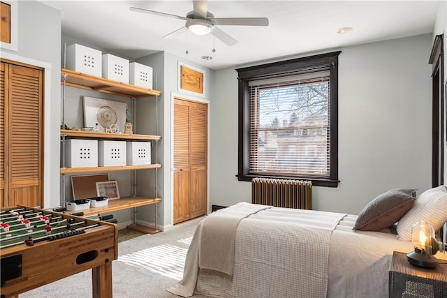 carpeted bedroom with a ceiling fan, radiator heating unit, baseboards, and multiple closets