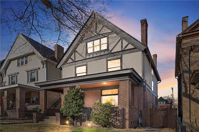 back of house at dusk featuring brick siding, stucco siding, a chimney, and fence