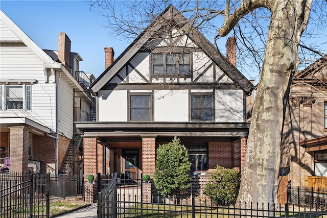 tudor-style house with a fenced front yard, brick siding, a porch, and stucco siding