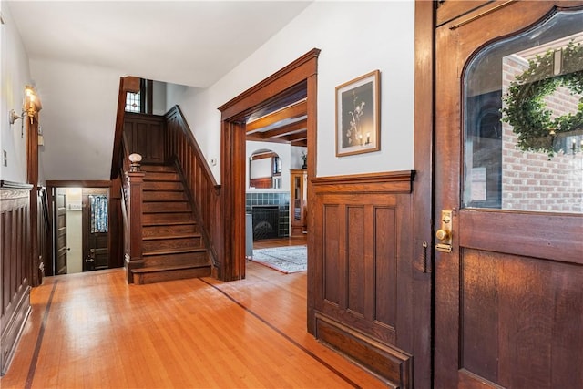 entryway featuring a tiled fireplace, light wood-style flooring, stairs, and wainscoting