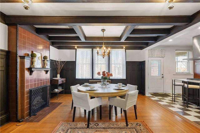 dining area featuring beamed ceiling, a notable chandelier, coffered ceiling, and a tile fireplace