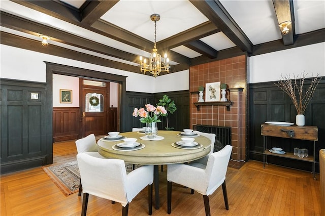 dining space with a wainscoted wall, beam ceiling, light wood-style floors, a decorative wall, and a chandelier