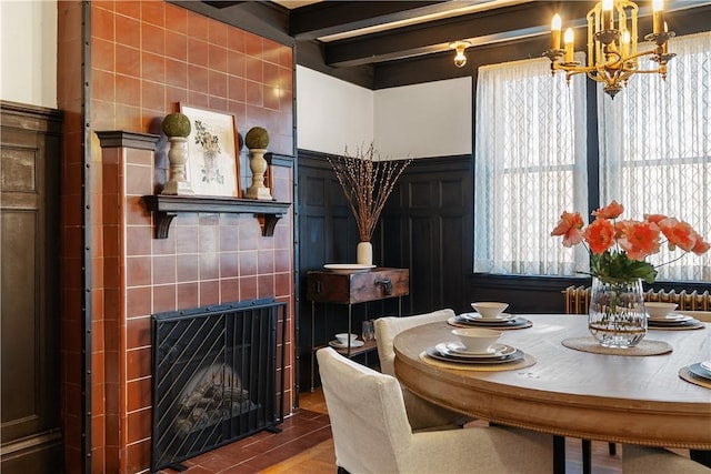 dining area featuring an inviting chandelier, beam ceiling, wood finished floors, and a fireplace