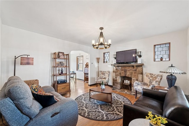 living area featuring baseboards, light wood-type flooring, a stone fireplace, an inviting chandelier, and arched walkways