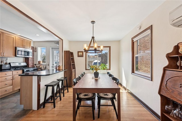 dining room with an AC wall unit, baseboards, light wood finished floors, and a chandelier