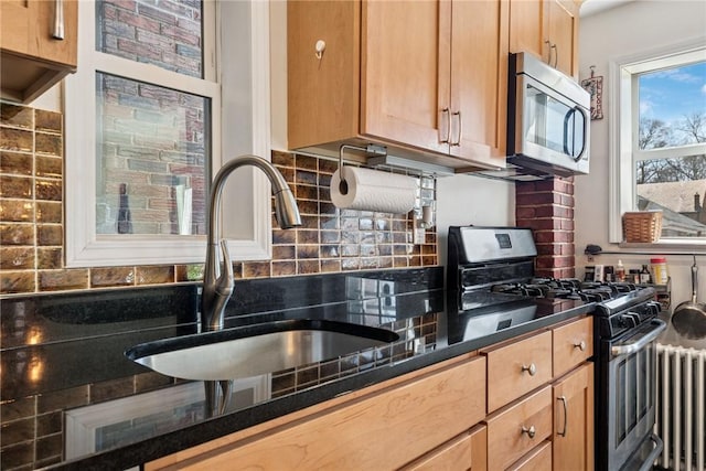 kitchen featuring radiator, a sink, decorative backsplash, appliances with stainless steel finishes, and dark countertops