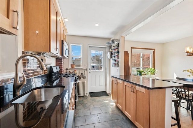 kitchen featuring stainless steel microwave, plenty of natural light, dark countertops, and gas range oven