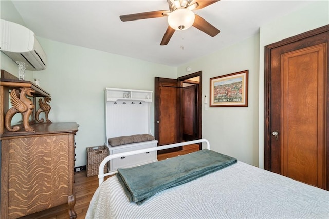 bedroom featuring a wall mounted AC, a ceiling fan, and wood finished floors