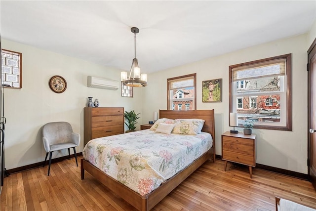 bedroom with an inviting chandelier, baseboards, light wood-style floors, and a wall unit AC