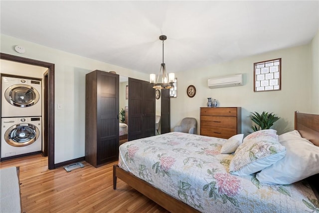 bedroom with baseboards, light wood-style floors, stacked washer and clothes dryer, a wall mounted air conditioner, and a chandelier