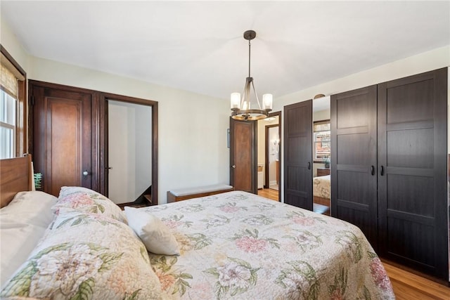 bedroom featuring an inviting chandelier, multiple windows, light wood-style floors, and a closet